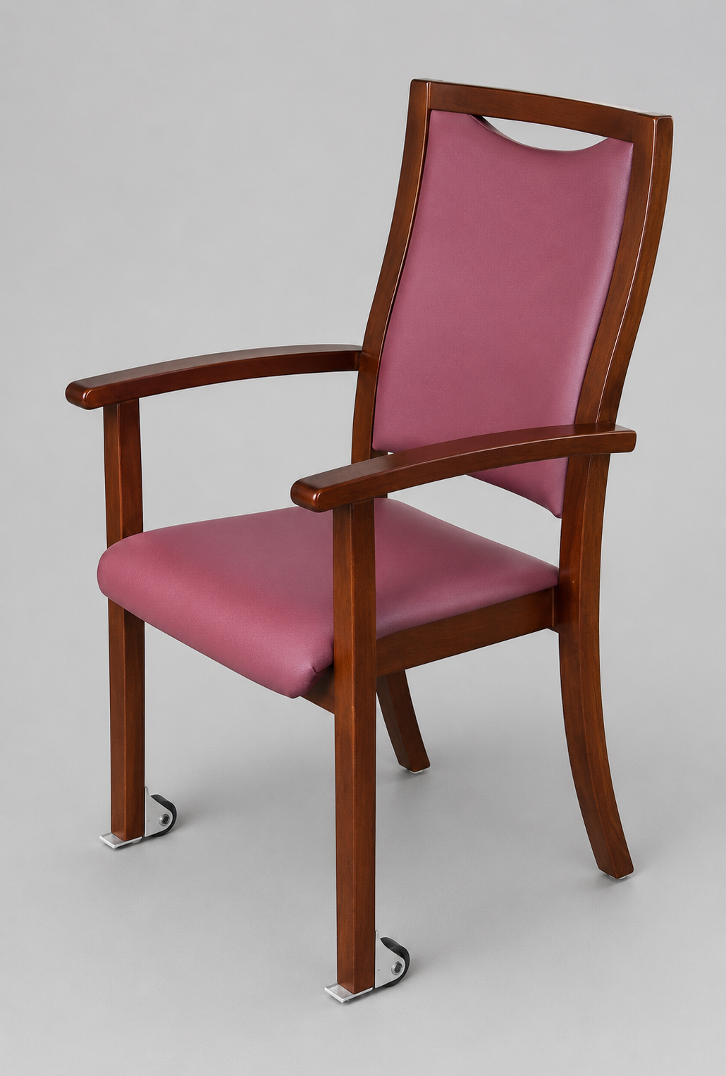 Ein Holzstuhl mit Armlehnen und rosa Polsterung ist mit einer Rolle von Rollendiscount mit Kippschutz (Rad-Ø 50 mm, weiche Lauffläche) ausgestattet, die über zwei Befestigungslöcher an den Vorderbeinen verfügt und für eine reibungslose Bewegung sorgt.